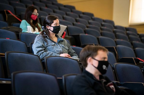 Three masked students listen attentively in class.