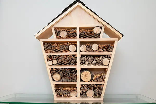 A bee hotel shaped like a house with a roof and a very tall rectangular body made up of smaller rectangles.